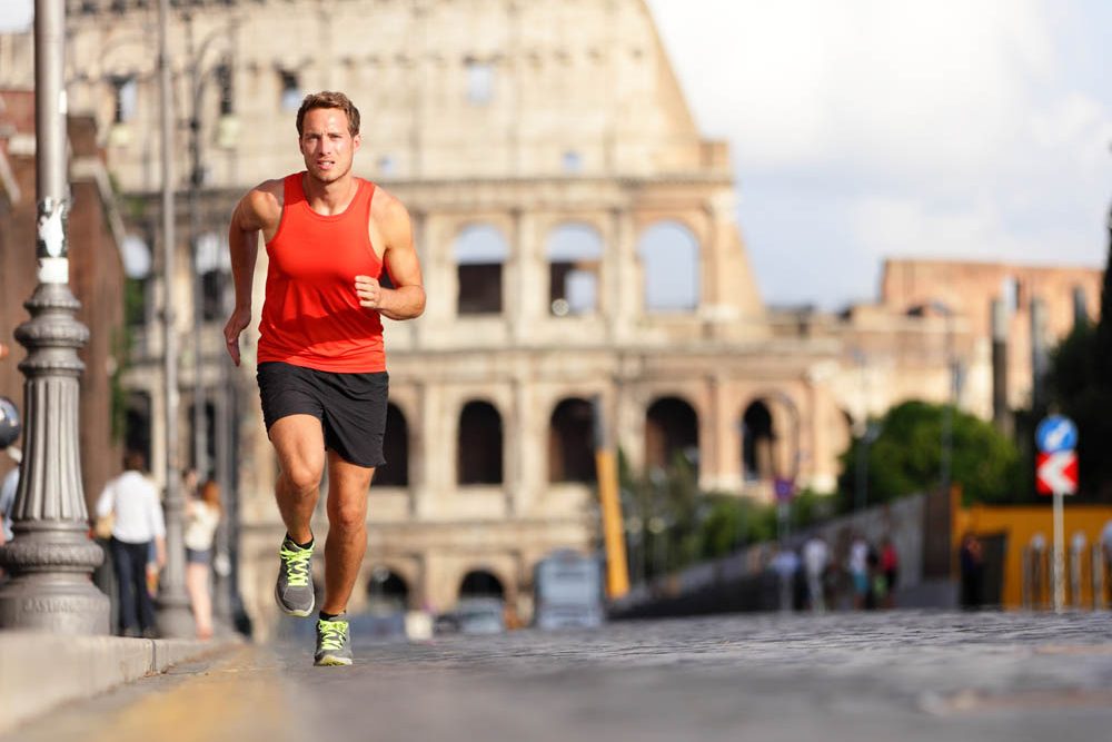 Running runner man by Colosseum, Rome, Italy. Male athlete training for marathon jogging in city of Rome in front of Coliseum in full body length. Fit male sport fitness model jogger in run outside.